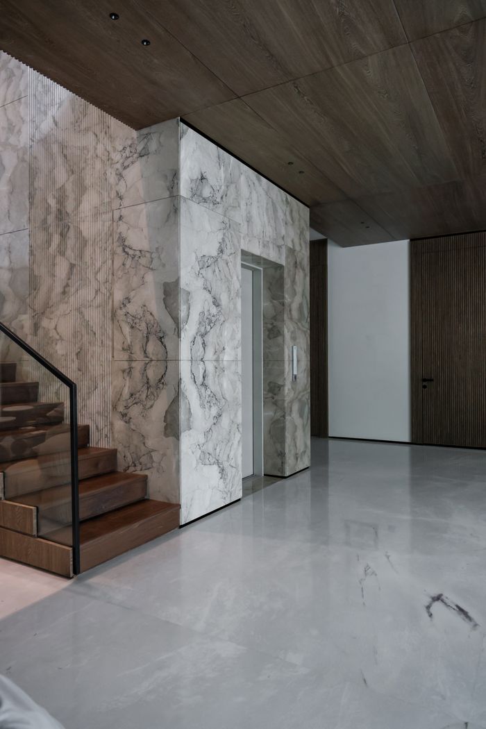 Sleek modern interior featuring marble walls and wooden staircase, exuding luxury.