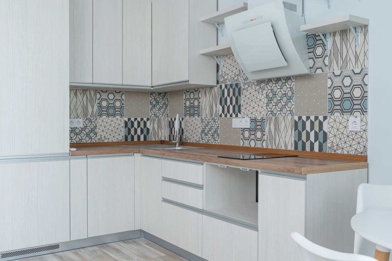 Interior of contemporary kitchen with white cabinets and wooden counter near ornamental tile on wall and modern appliances in apartment